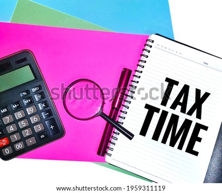 Tax time wording. Written on a note book with a magnifying glass, calculator and a pen on colorful A4 paper background.