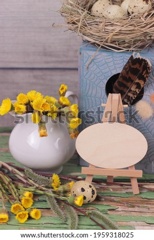 Beautiful spring easter greeting card with blooming coltsfoot, nest and birdhouse on rustic background.Springtime picture with empty blank wooden plaque for text.