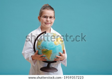 Portrait of little girl in white coat holding world map and smiling at camera against the blue background