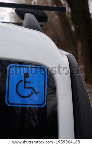 Disabled sign on a car. Blue sticker on the rear window of a white car.