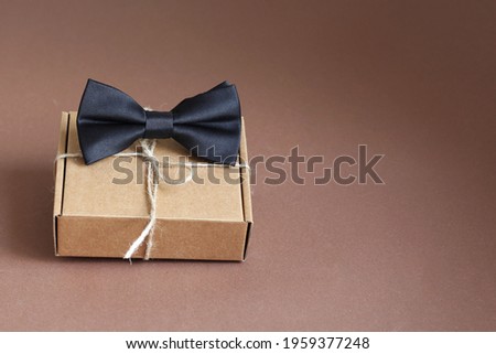 Elegant men's bow tie and gift on brown background. Concept of Father's Day and International Men's Day. Copy space. 