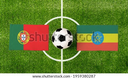 Top view ball with Portugal vs. Ethiopia flags match on green football field.