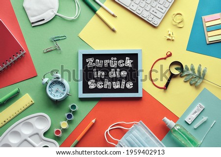 Zuruck in die Schule means or back to school in German language. Corona, covid schnelltest or quick tests, medical mask, stationary. Computer keyboard. Flat lay on layered colored paper background.