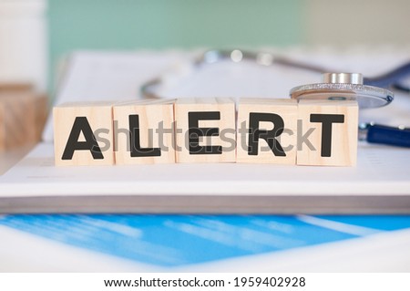 The word alert is written on wooden cubes near a stethoscope on a paper background. Medical concept.