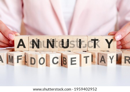 Hands hold a wooden cube with the word annuity standing on top of other cubes with letters, pink background