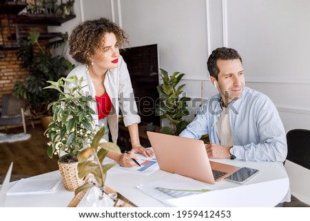 Concentrated business partners thinking about project ideas, working together in modern office. Stylish serious colleagues using laptop, learning financial graphs for making report, teamwork concept