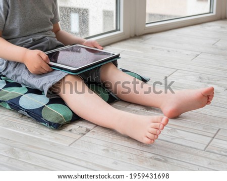 Curious boy watch cartoons on digital tablet. Kid sits on floor and uses electronic device. Indoor leisure for children while it's raining outside.