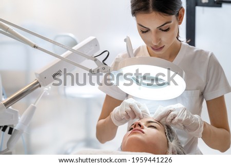 Skin treatment, beautician squeezing pimples from face of young female. Cleansing facial skin, beautician squeezed blackheads. Royalty-Free Stock Photo #1959441226