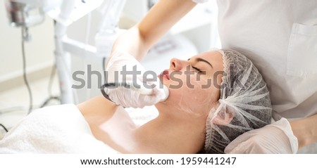 The doctor applies a special gel to the patient. Anti acne phototherapy with professional equipment. Beautiful woman during photo rejuvenation procedure. Face skin treatment at beauty salon.