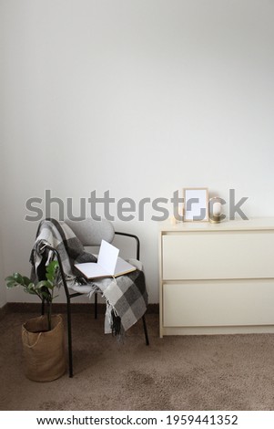 Stylish composition of bedroom interior with wooden commode and comfortable armchair. Cozy home decor.