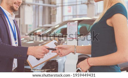 Car salesman sells a car to happy customer in car dealership and hands over the keys