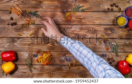 The chef's hand lays out Bell peppers, cloves, spices, garlic and coarse table salt on a brown wooden background. Flat layout. copy space.