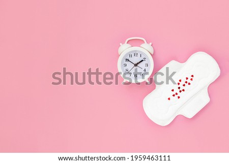Female monthly pads and white alarm clock on pink background. Concept of women's health and regular menstruation. Copy space