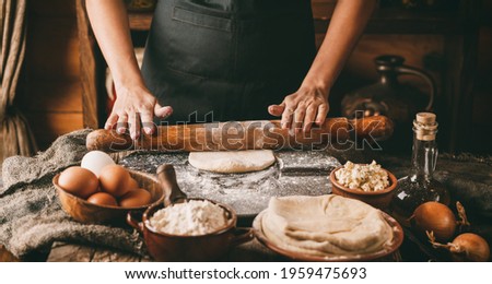 Woman hands rolls the dough with a rolling pin on rustic wooden background. Cooking bread with cheese, eggs and herb. Homemade healthy food concept, toning
