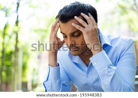 Closeup portrait, stressed young business man, hands on head with bad headache, isolated background of trees outside. Negative human emotion facial expression feelings. Royalty-Free Stock Photo #195948383