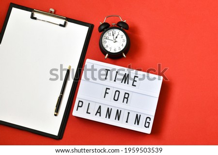 Light box with the text TIME FOR PLANNING near a black alarm clock and clipboard on a red background. Copy space, flat lay.