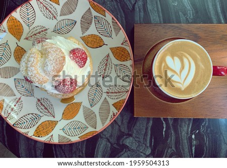 top view of a cup of coffee red color cup with hot latte art in heart shape on wooden trey with creme cake strawberry on top in nice plate