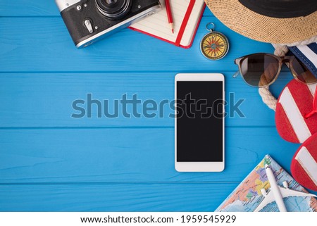 Above photo of camera notebook pencil compass hat sunglasses sandals map phone and airplane isolated on the blue background with empty space