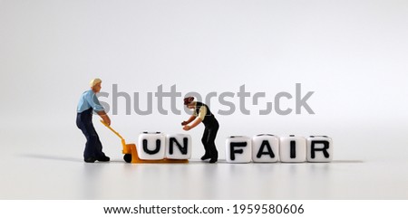 Two miniature men moving the cube of 'UN' word from cube with 'FAIR' word to cart. White cube with words and miniature people. Royalty-Free Stock Photo #1959580606