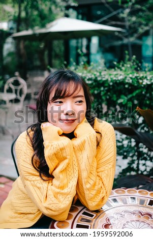 Close up of young pretty Asian woman in blue yellow sweater with garden background.