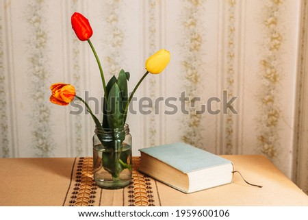 Three red and yellow tulips in the glass jar and a book. Retro vibes. Copy space