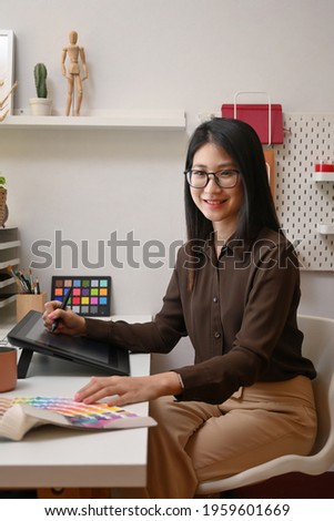 Portrait of cheerful young woman graphic designer sitting in office  and smiling to camera.