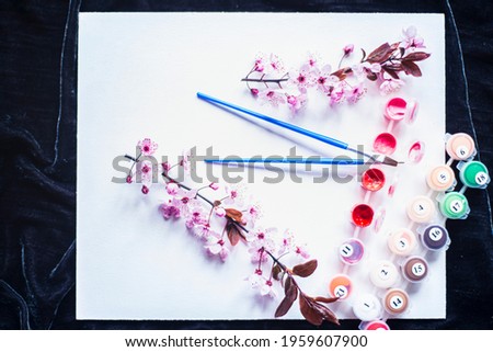 blank paper brushes and pink paints and spring pink flowers, paints in tubes with flower numbers and brushes on white canvas, paintings by numbers and a branch with fresh flowers in delicate paints