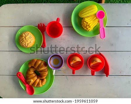Top view of artificial food and drinks (kid toys) served on a white wooden table.