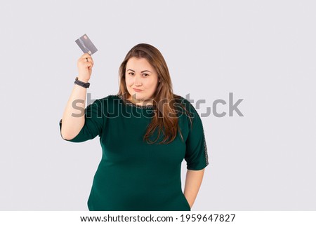 Very proud smug businesswoman wearing green dress showing credit card over grey background. Confident banker, plus size woman showing your sale promotion. . High quality photo