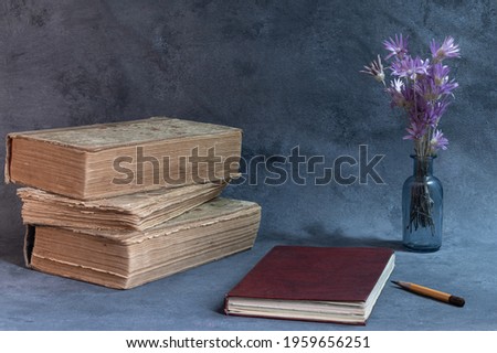 Three vintage books and a closed notebook on a table on a blue background.