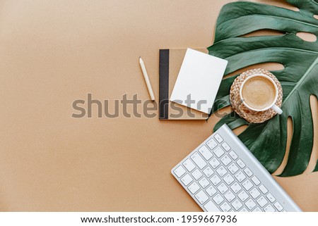 A simple trendy office Desk. Coffee cup, monstera leaf, blank card and notebook .Home Office desktop with space copying. Top view, copy space. Minimal concept 