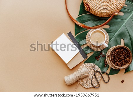 Womens accessories, Ratan bag, straw hat, leaves monstera, coffee cup and blank note on brown background. Flat lay, top view