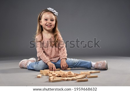 Little girl playing with wooden cubes on gray background
