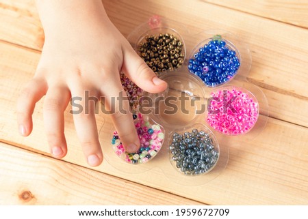 The child makes jewelry with his own hands, stringing colorful beads on a thread.