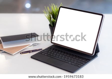 Work area tablet blank white screen  with notepad a placed  table at the office.