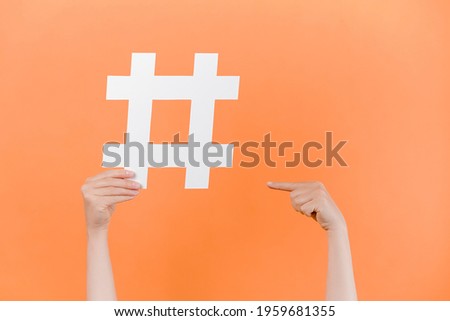 Horizontal images of female hands holding and pointing on large big hashtag sign, viral web content, internet promotion, isolated on pastel orange studio wall. Blogging blog website strategy concept Royalty-Free Stock Photo #1959681355