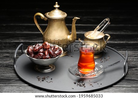 Composition with glass of tasty Turkish tea and dates on dark wooden background