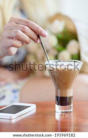 woman with hot cup of coffee and cell phone laying on the table in a cafe