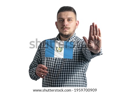 White guy holding a flag of Guatemala and with a serious face shows a hand stop sign isolated on a white background.