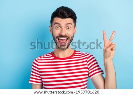 Photo of cheerful handsome young man show v-sign excited good mood isolated on pastel blue color background
