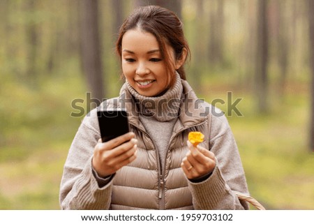 technology, leisure and people concept - young asian woman with smartphone using app to identify mushroom in autumn forest