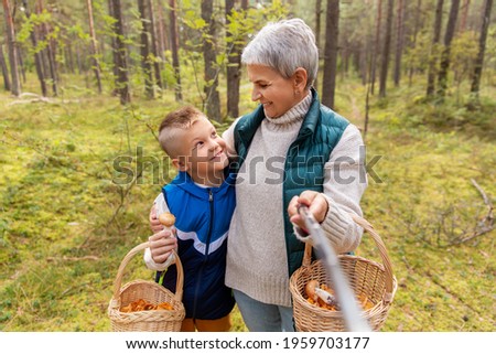picking season, leisure and people concept - happy smiling grandmother and grandson with mushrooms in baskets taking picture with selfie stick in forest