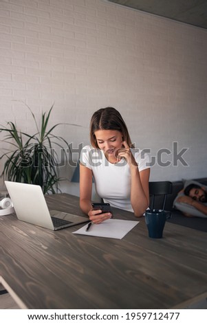Happy ambitious woman working from home. She is sitting at her desk and using cell with a big smile on her face