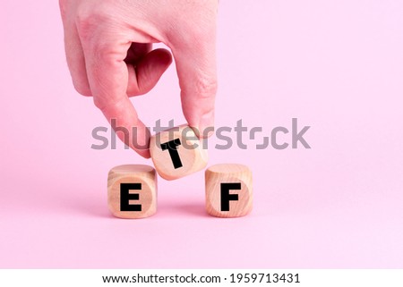 A male hand adding the letter T to make the word ETF with wooden cubes on a pink background