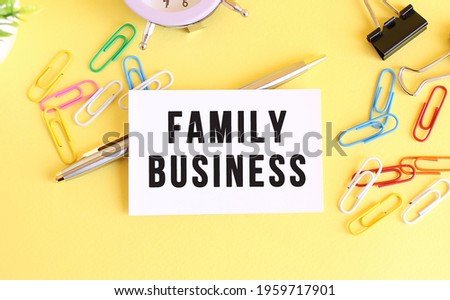 Top view of a business card with text FAMILY BUSINESS, pen, paper clips and clock on a yellow background. Business concept.