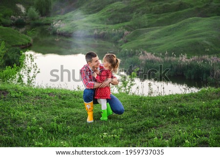 dad with little daughter in bright colored rubber boots on a walk by the lake on dad's day