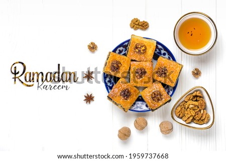 Traditional arabic dessert baklava with walnuts, raisins on plate, bowl of tea with Uzbek national ornament on white wooden table Text Happy Nowruz Holiday Concept of spring came Top view Flat lay