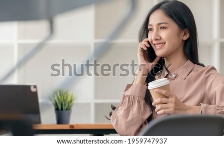 Portrait of beautiful asian woman holding cup of coffee and using smartphone while sitting at the table in cafe.