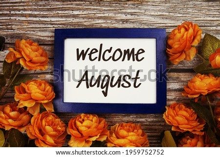 Welcome August text in blue border frame with flower decoration on wooden background