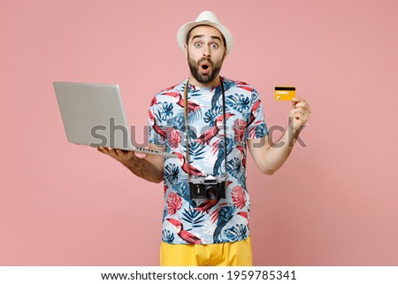 Shocked traveler tourist man in summer clothes hat using laptop pc computer booking hotel hold credit bank card isolated on pink background. Passenger travel on weekends. Air flight journey concept